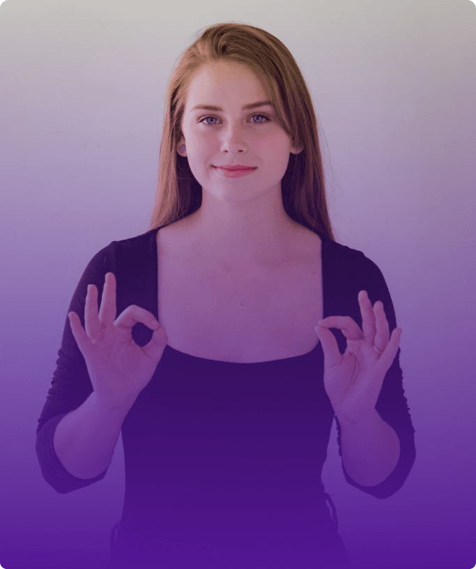 Beyaz bir duvarın önünde duran, uzun sarı saçlı, mavi gözlü ve siyah kazaklı; Baş parmağını ve işaret parmağını birleştirerek işaret dilinde 'sıfır'  yapan bir kız var.